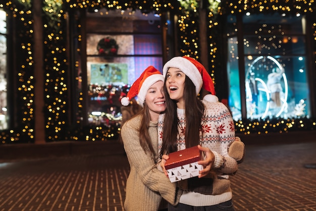 Retrato de felices lindos jóvenes amigos abrazándose y sonriendo mientras camina en la víspera de Navidad al aire libre.