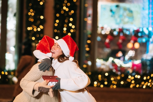 Retrato de felices lindos jóvenes amigos abrazándose y sonriendo mientras camina en la víspera de Navidad al aire libre.