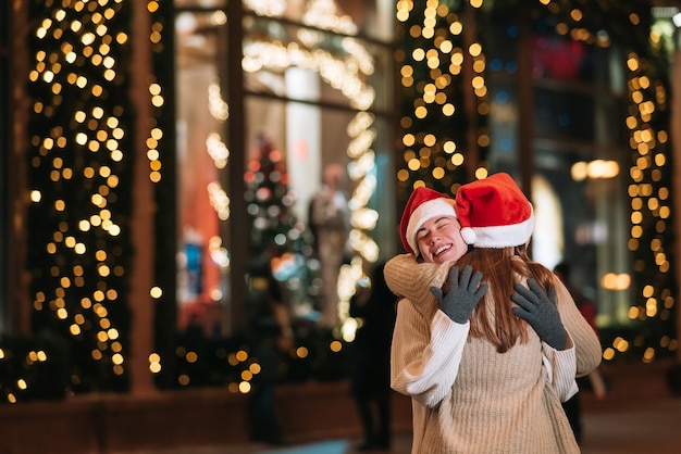 Retrato de felices lindos jóvenes amigos abrazándose y sonriendo mientras camina en la víspera de Navidad al aire libre.
