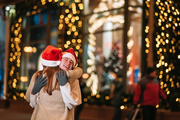 Retrato de felices lindos jóvenes amigos abrazándose y sonriendo mientras camina en la víspera de Navidad al aire libre.