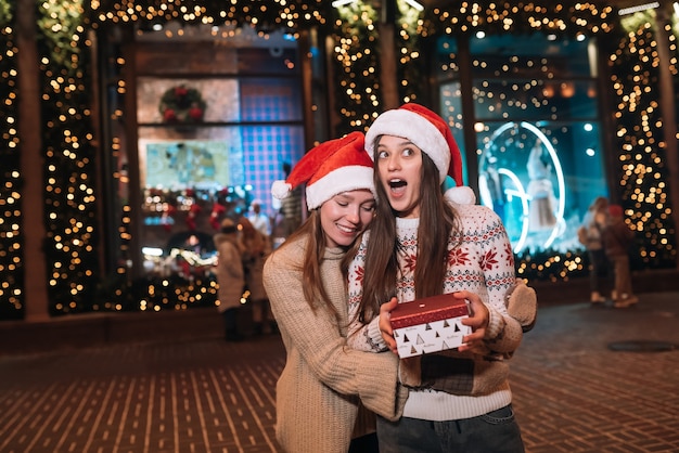 Retrato de felices lindos jóvenes amigos abrazándose y sonriendo mientras camina en la víspera de Navidad al aire libre.