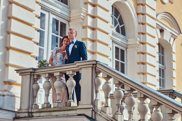 Retrato de felices recién casados abrazándose mientras posan en las escaleras del hermoso palacio antiguo.