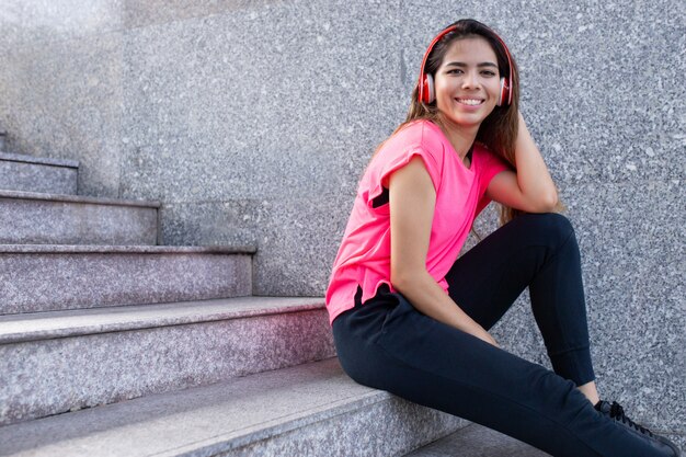 Retrato de feliz adolescente sentado en las escaleras en los auriculares