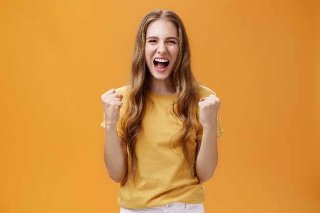 Retrato de feliz alegre joven afortunada europea con largo cabello ondulado natural levantando los puños ...