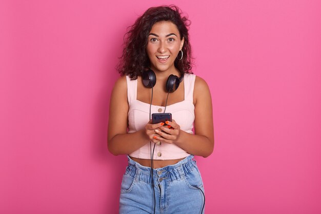 Retrato de feliz bella mujer joven con teléfono en la mano y sonriente, vistiendo ropa casual