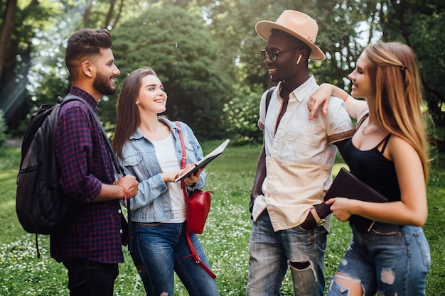 Retrato de feliz dos jóvenes y dos mujeres hablando al aire libre en la universidad en el campus