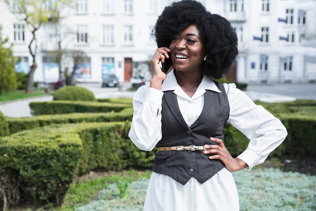Retrato feliz de una empresaria joven africana con su mano en las caderas que habla en el teléfono móvil