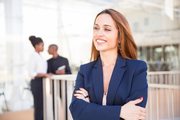 Retrato de feliz empresaria y sus empleados en segundo plano