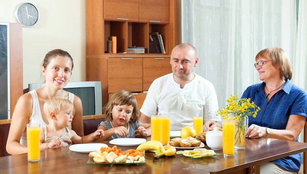 Retrato de feliz familia multigeneración comiendo friuts con jugo en casa juntos