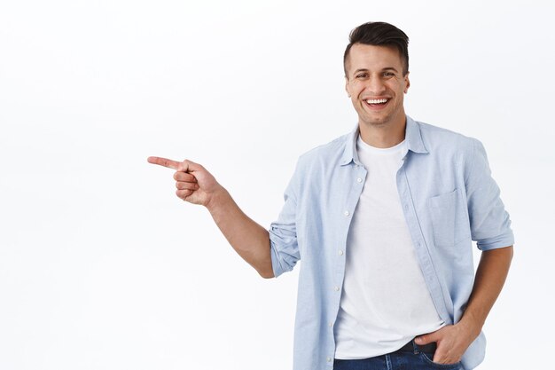 Retrato de feliz, guapo hombre adulto masculino apuntando con el dedo hacia la izquierda y sonriendo, recomendar servicio o producto