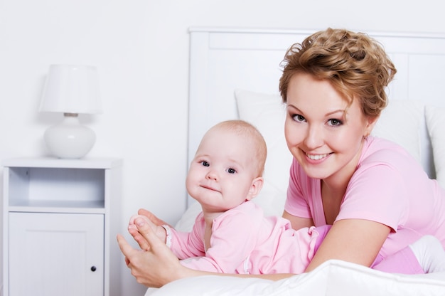 Retrato de feliz hermosa joven madre acostada con su bebé en la cama