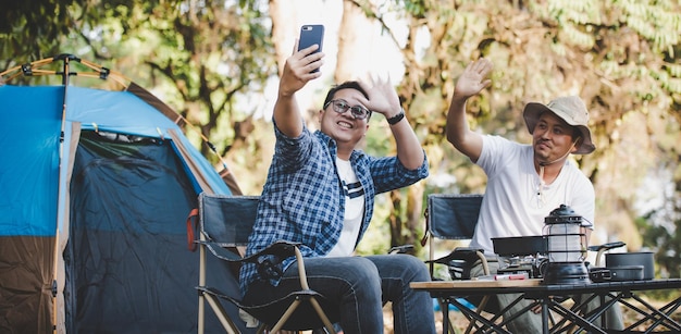 Retrato feliz hombre asiático amigos Hacer una videollamada con un teléfono inteligente en el campamento Juego de cocina en el frente Cocina al aire libre Viajar acampar concepto de estilo de vida