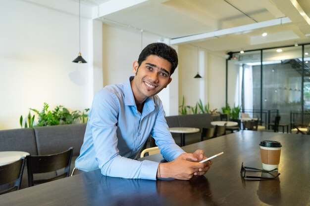 Retrato de feliz joven empresario indio sentado en el café.