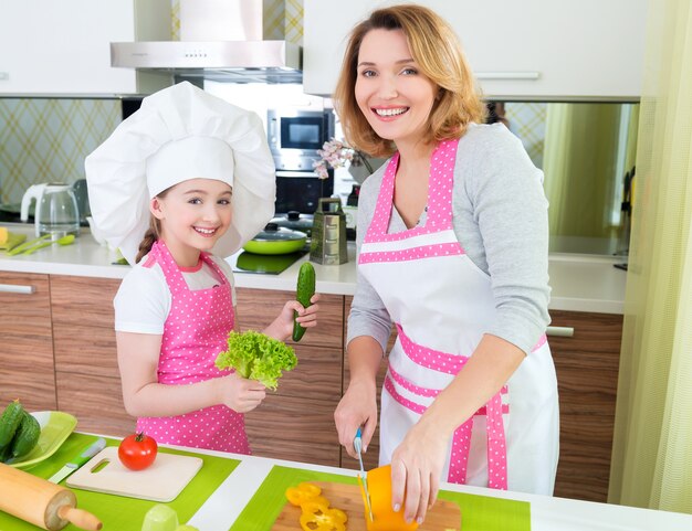 Retrato de feliz joven madre con hija en delantal rosa cocinando en la cocina.