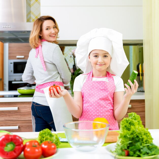 Retrato de feliz joven madre con hija en delantal rosa cocinando en la cocina.