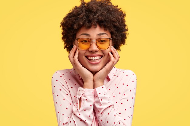 Retrato de feliz joven negra tiene una agradable sonrisa tierna con dientes, sostiene la barbilla