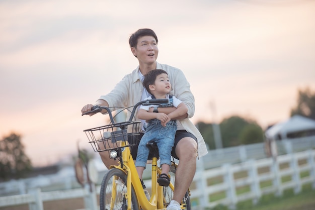 Retrato de feliz joven padre e hijo en bicicleta. padre e hijo jugando en el parque a la hora del atardecer. gente divirtiéndose en el campo. concepto de familia amistosa y de vacaciones de verano.