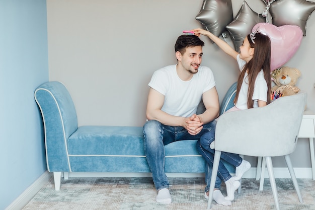 Retrato de feliz linda hijita caucásica y su apuesto padre jugando juntos en el dormitorio