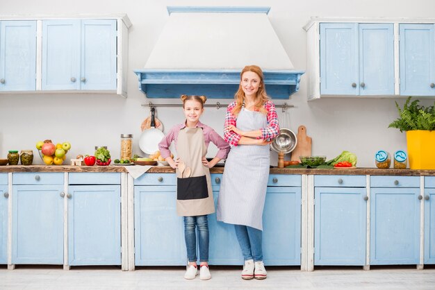 Retrato de feliz madre e hija en delantal de pie en la cocina