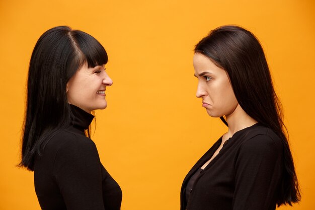 Un retrato de una feliz madre e hija en el estudio sobre fondo dorado. Colores de moda. Concepto de expresiones faciales y emociones positivas humanas. Vista de perfil