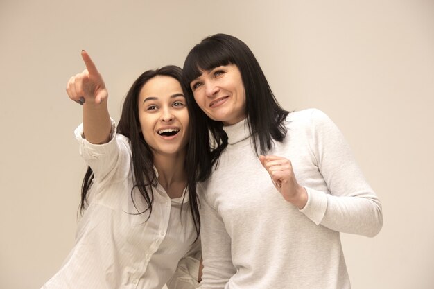 Un retrato de una feliz madre e hija en el estudio sobre fondo gris. Concepto de expresiones faciales y emociones positivas humanas