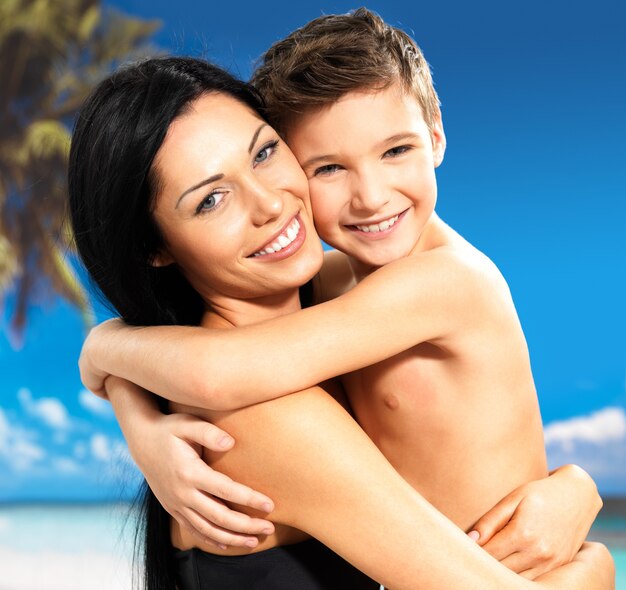 Retrato de feliz madre sonriente abraza a su hijo de 8 años en la playa tropical