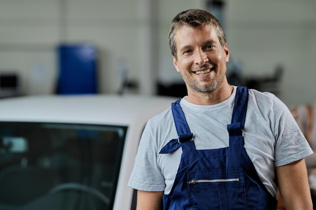 Retrato de feliz mecánico de automóviles en taller de reparación de automóviles mirando a la cámara