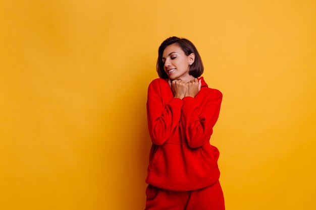 Retrato de feliz mujer bronceada en forma vistiendo pantalones y sudadera con capucha de lana roja cálida de moda, preparándose para el frío invierno