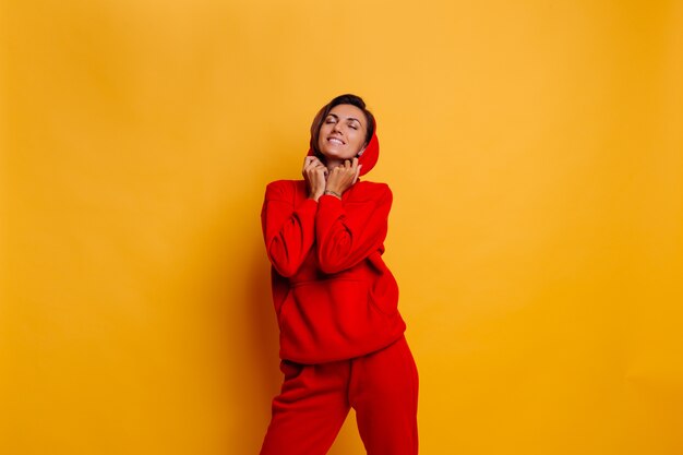 Retrato de feliz mujer bronceada en forma vistiendo pantalones y sudadera con capucha de lana roja cálida de moda