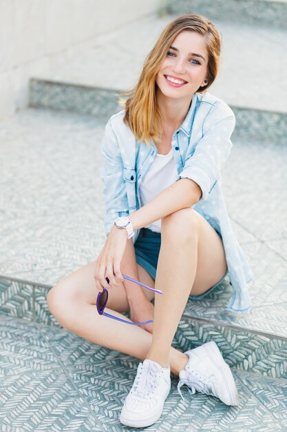 Retrato de una feliz mujer caucásica joven sentada en gris claro