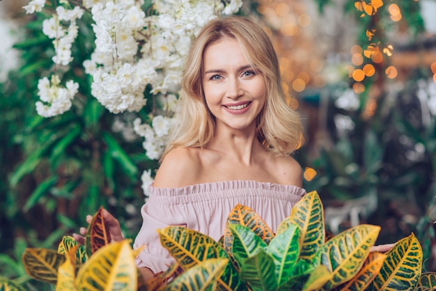 Foto gratuita retrato feliz de una mujer joven rubia que se coloca delante de las hojas amarillas y verdes