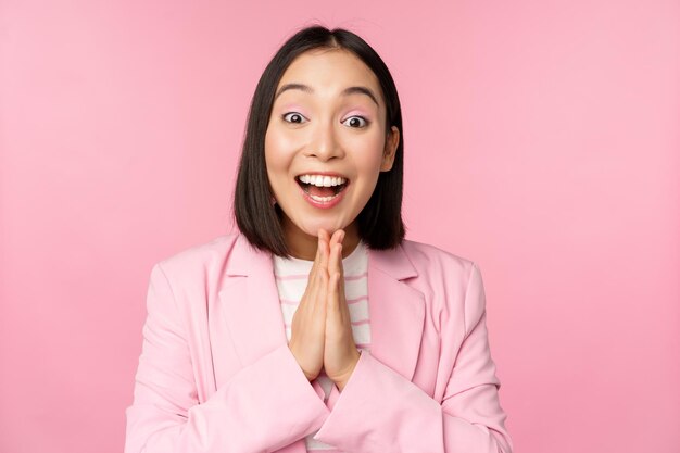 Retrato de la feliz mujer de negocios asiática de la oficina, directora general, en traje regocijándose y riéndose ganando celebrando alcanzar el objetivo y regocijándose de pie sobre un fondo rosa