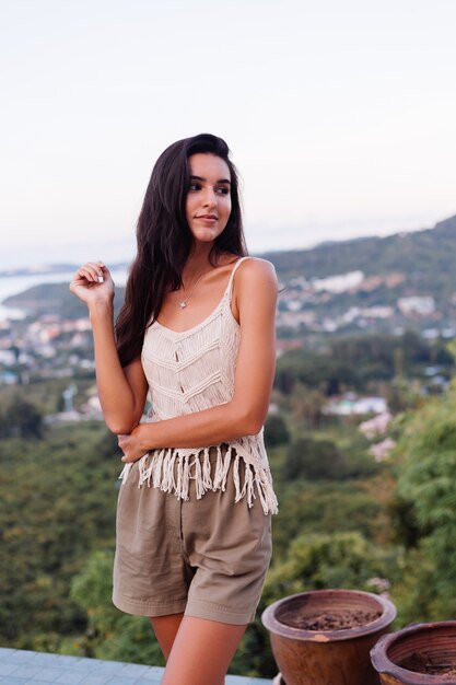 Retrato de feliz mujer romántica tranquila caucásica en look casual con el pelo largo con aretes y collar sobre fondo increíble vista hermosa en montañas verdes