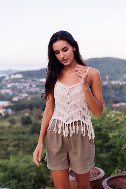 Retrato de feliz mujer romántica tranquila caucásica en look casual con el pelo largo con aretes y collar sobre fondo increíble vista hermosa en montañas verdes