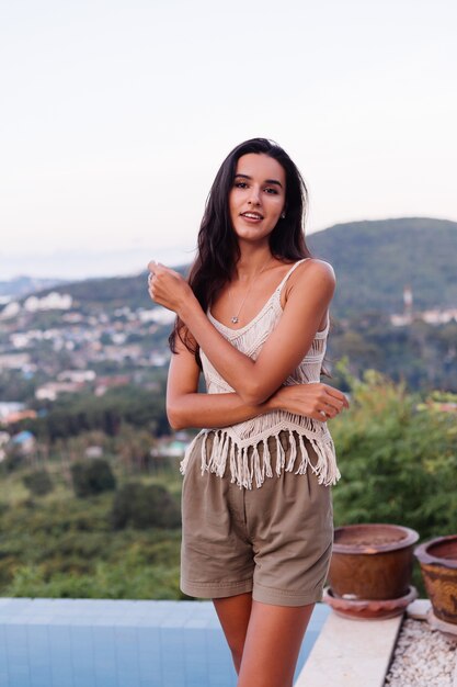 Retrato de feliz mujer romántica tranquila caucásica en look casual con el pelo largo con aretes y collar sobre fondo increíble vista hermosa en montañas verdes