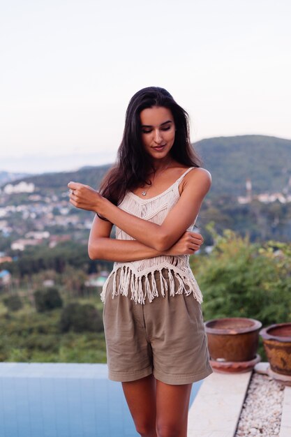 Retrato de feliz mujer romántica tranquila caucásica en look casual con el pelo largo con aretes y collar sobre fondo increíble vista hermosa en montañas verdes