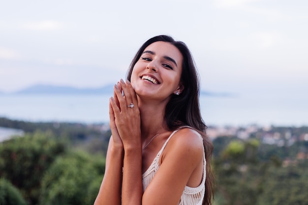 Retrato de feliz mujer romántica tranquila caucásica en look casual con el pelo largo con aretes y collar sobre fondo increíble vista hermosa en montañas verdes