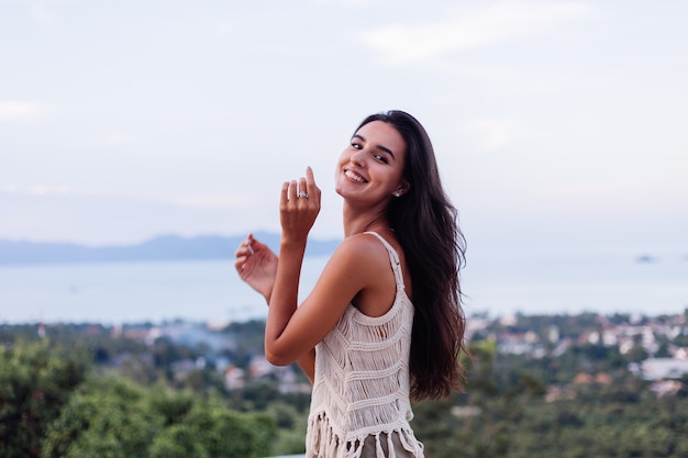 Retrato de feliz mujer romántica tranquila caucásica en look casual con el pelo largo con aretes y collar sobre fondo increíble vista hermosa en montañas verdes