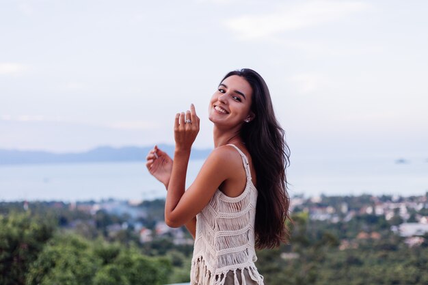 Retrato de feliz mujer romántica tranquila caucásica en look casual con el pelo largo con aretes y collar sobre fondo increíble vista hermosa en montañas verdes