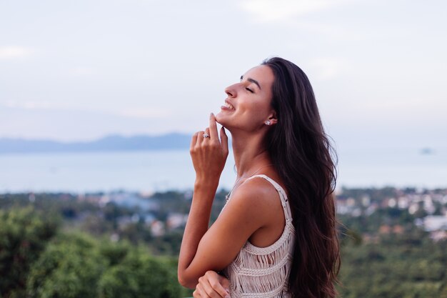 Retrato de feliz mujer romántica tranquila caucásica en look casual con el pelo largo con aretes y collar sobre fondo increíble vista hermosa en montañas verdes