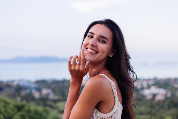 Retrato de feliz mujer romántica tranquila caucásica en look casual con el pelo largo con aretes y collar sobre fondo increíble vista hermosa en montañas verdes