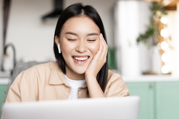 Retrato de feliz niña asiática habla en el chat de video que se comunica con la aplicación de la computadora portátil riendo y ...
