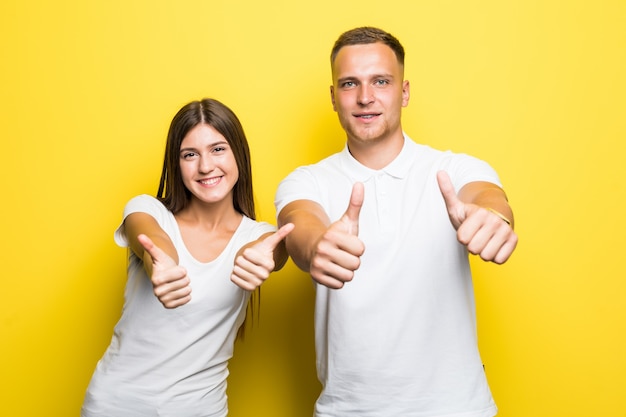 Retrato de la feliz pareja joven mostrando los pulgares para arriba aislado en amarillo