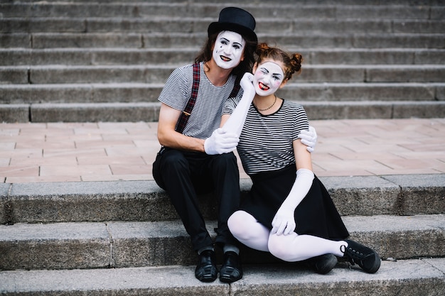 Retrato de una feliz pareja mime sentado en la escalera