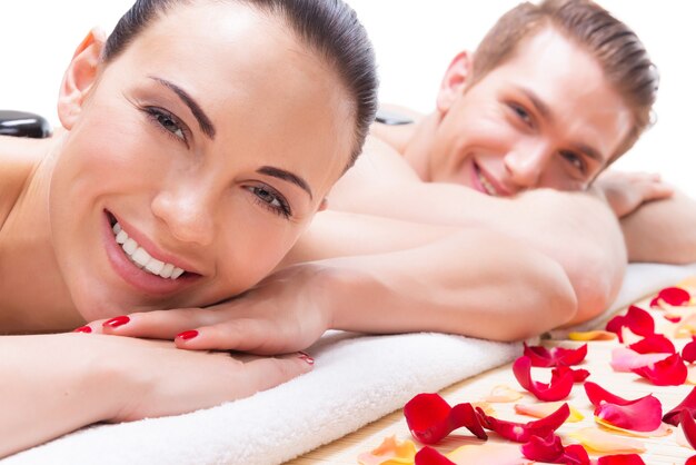 Retrato de feliz pareja sonriente relajante en el salón de spa con piedras calientes en el cuerpo.