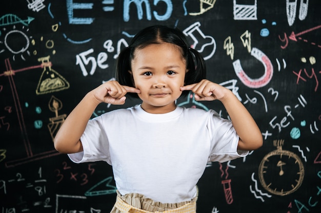 Retrato de feliz pequeño alumno de pie en la parte delantera de la pizarra de educación con una postura encantadora