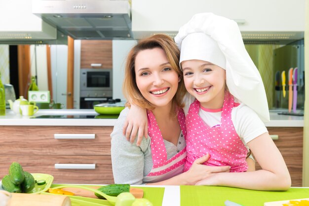 Retrato de feliz sonriente madre e hija en delantal rosa en la cocina.