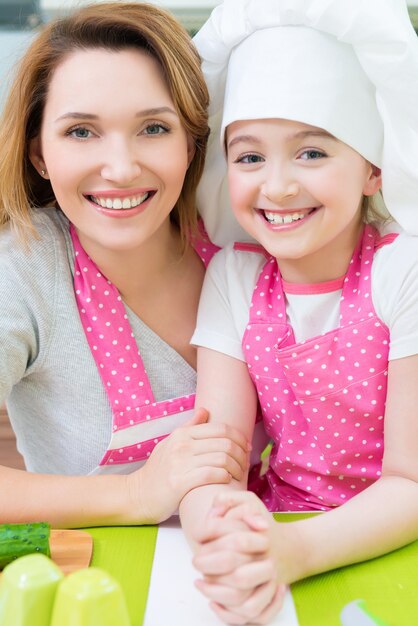 Retrato de feliz sonriente madre e hija en delantal rosa en la cocina