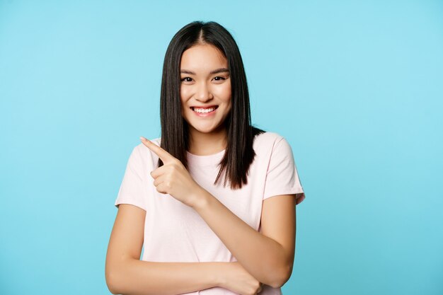 Retrato de feliz sonriente modelo femenino asiático apuntando a la esquina superior izquierda mostrando banner de venta tienda ...