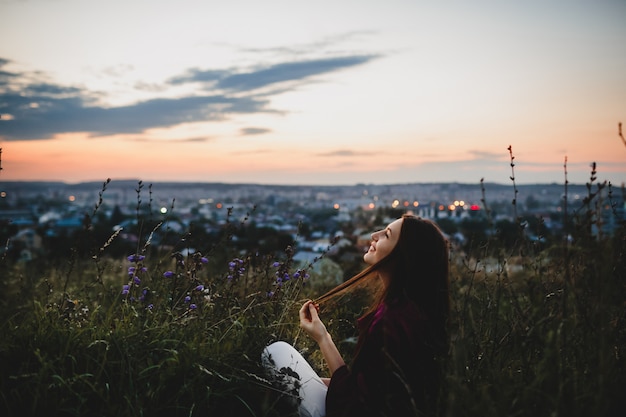 Retrato femenino, la naturaleza. Mujer en camisa violeta se sienta en la hierba